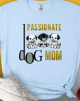 The Dog Mom Series, Volume 6 unisex T-shirt is light blue and made from 100% cotton. It features Passionate Dog Mom text with three illustrated puppies. Perfect for any dog lover. Designed by Dog Gang.