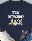 The Easily Distracted By Dogs Series, Volume 1, Womens T-Shirt in navy displays the words Easily Distracted by Dogs in white and gold, accompanied by charming dog illustrations: a Dalmatian, a Golden Retriever, a Pug, a Poodle, Dachshund, French Bulldog, English Bulldog, Chihuahua, Husky and more. Designed by Dog Gang.