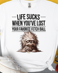 Das weiche Unisex-T-Shirt in Weiß zeigt eine zottelige Hundegrafik mit dem Text „Life Sucks When You've Lost Your Favorite Fetch Ball. Aus 100 % Baumwolle. Design von Dog Gang.