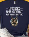 Das Unisex-T-Shirt zeigt einen witzig gezeichneten depressiven Deutschen Schäferhund und den lustigen Spruch„Life Sucks When You've Lost Your Favorite Fetch Ball“. Design von Dog Gang.