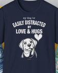 Shirtdesign by Dog Gang: This navy blue t-shirt features an adorable dog illustration accompanied by the playful white text, My Dog Is Easily Distracted By Love & Hugs. Crafted from soft-style, 100% cotton, this unisex tee provides exceptional comfort for pet enthusiasts.