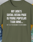 Das Unisex-T-Shirt in Militärgrün besteht aus 100 % Baumwolle und trägt den humorvollen Slogan: „Die Social-Media-Seite meines Hundes ist beliebter als meine.“ Design von Dog Gang.