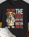 Dieses schwarze Unisex-T-Shirt zeigt einen witzigen Comic-Hund im Arztmantel mit dem Spruch „Walking The Dog Every Day Keeps The Doctor Away“. Design von Dog Gang.