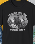 Western Style Volume 3 Unisex T-Shirt has a cowboy scene with humorous elements, perfect for any dog lover. Designed by Dog Gang.