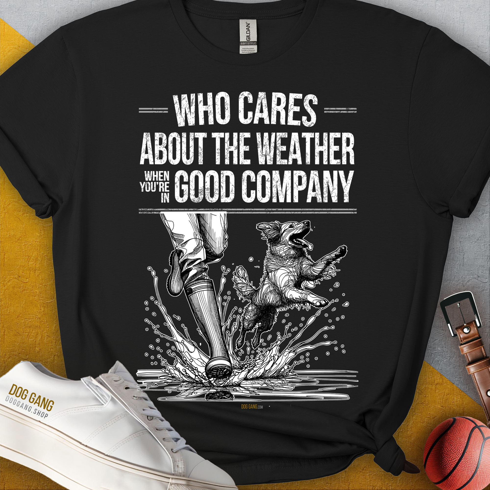Das „Who Cares About The Weather When Youre In Good Company, Volume 1, Unisex-T-Shirt“ ist aus schwarzer, ringgesponnener Baumwolle und zeigt Menschenbeine in Stiefelnund einen plantschenden Hund. Design von Dog Gang.