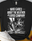 Das „Who Cares About The Weather When Youre In Good Company, Volume 1, Unisex-T-Shirt“ ist aus schwarzer, ringgesponnener Baumwolle und zeigt Menschenbeine in Stiefelnund einen plantschenden Hund. Design von Dog Gang.