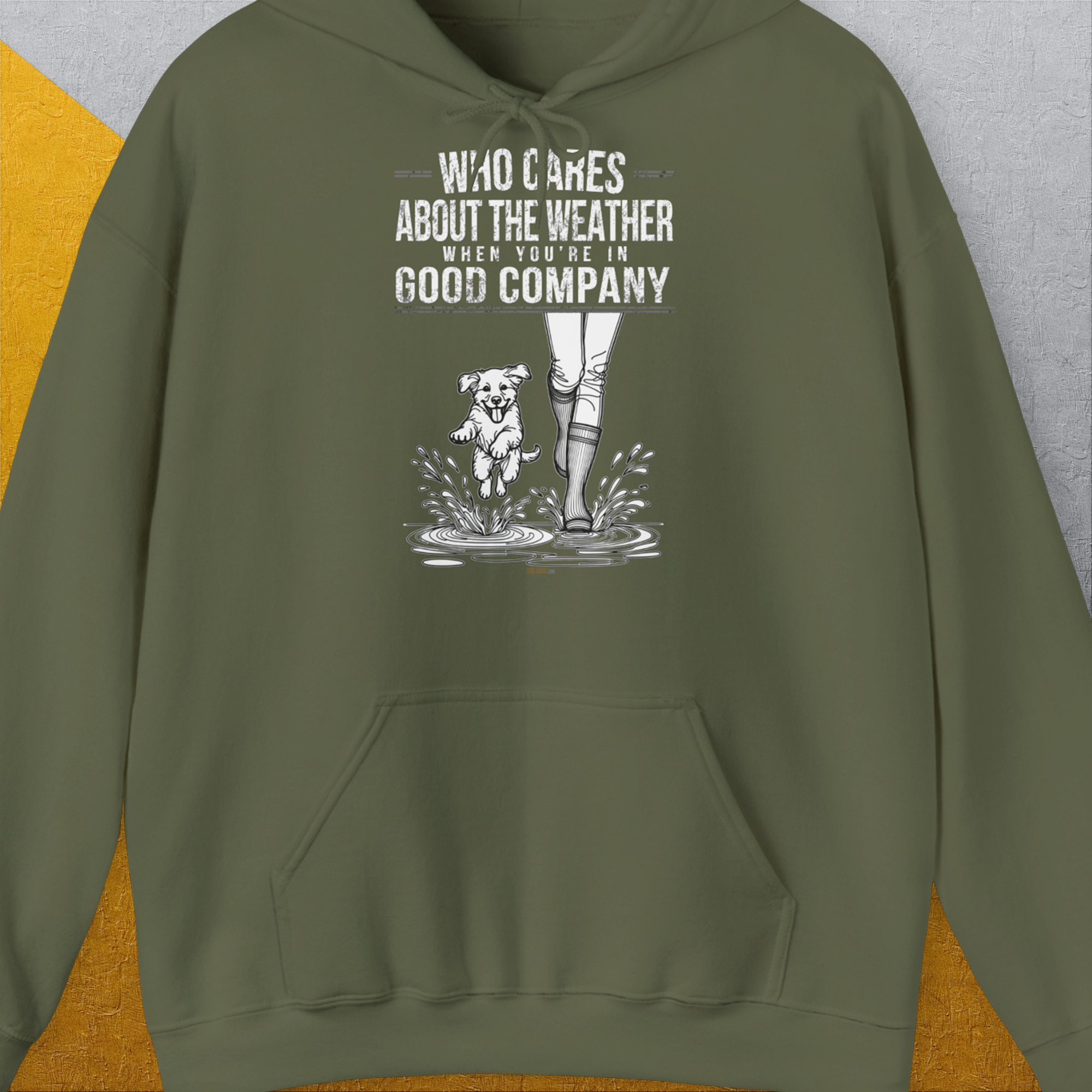 Der Unisex-Kapuzenpullover in Militärgrün zeigt eine verspielte Grafik eines Hundes und einer Person von der man nur die Regenstiefel sieht, mit dem Spruch „Who Cares About The Weather When You're In Good Company?“. Entworfen von Dog Gang.