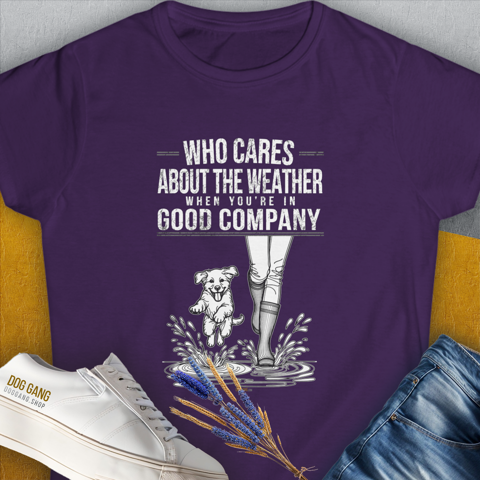 Purple Womens T-Shirt with a funny dog and boots splashing in water. Saying: Who Cares About The Weather When Youre In Good Company, Volume 2. Designed by Dog Gang.