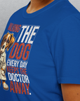 Jemand trägt ein blaues Unisex-T-Shirt mit dem Titel „Walking The Dog Every Day Keeps The Doctor Away, Volume 1“. Es besteht aus 100 % Baumwolle, zeigt einen Cartoon-Hund und verspricht Komfort und Stil für jedermann.