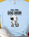 Soft light blue tee with Full Time Dog Mom and a cartoon puppy on a tricycle, playfully surrounded by a ball and shoes—ideal for any dog person. Designed by Dog Gang.