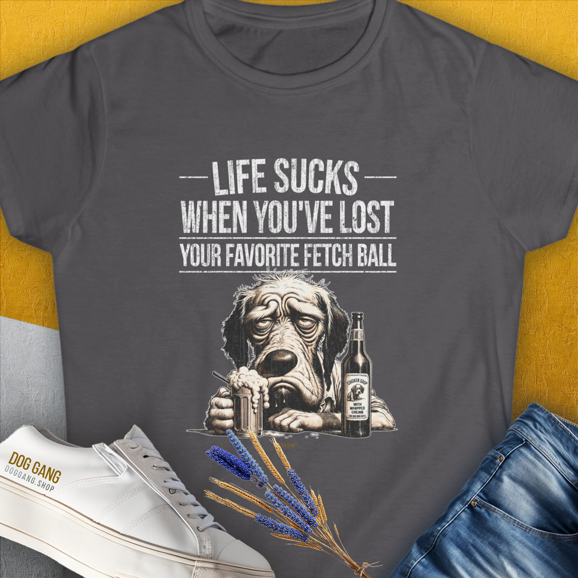 Charcoal t-shirt "Life Sucks When You've Lost Your Favorite Fetch Ball", Volume 5 from the popular series of the same name. Funny drawing of a depressed dog face. Next to the dog is a full glass and a bottle with a label that says "Chicken Soup with Whipped Cream, for Sad Dog Days". Designed by Dog Gang.
