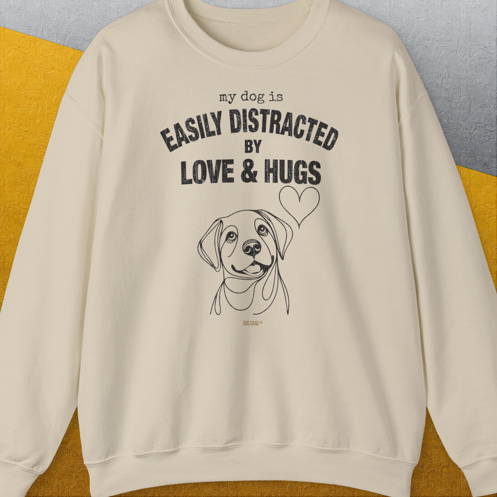 Unisex sand sweatshirt, ethically crafted from cotton, showcases My Dog is Easily Distracted by Love & Hugs text with a delightful dog and heart illustration. Designed by Dog Gang.