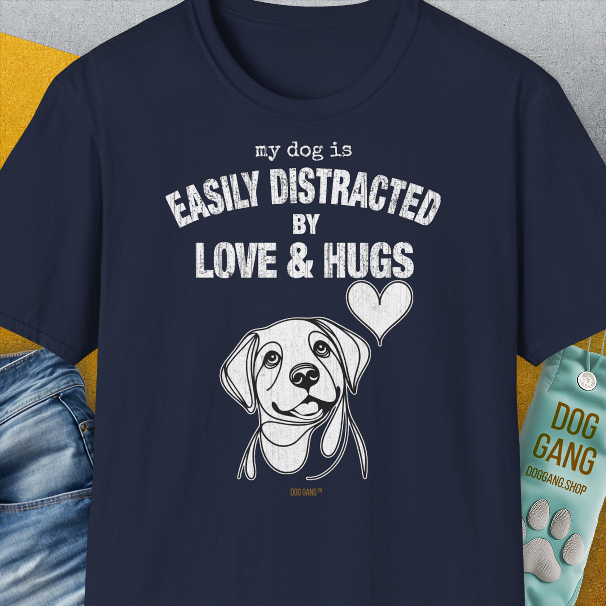 Shirtdesign by Dog Gang: This navy blue t-shirt features an adorable dog illustration accompanied by the playful white text, My Dog Is Easily Distracted By Love & Hugs. Crafted from soft-style, 100% cotton, this unisex tee provides exceptional comfort for pet enthusiasts.
