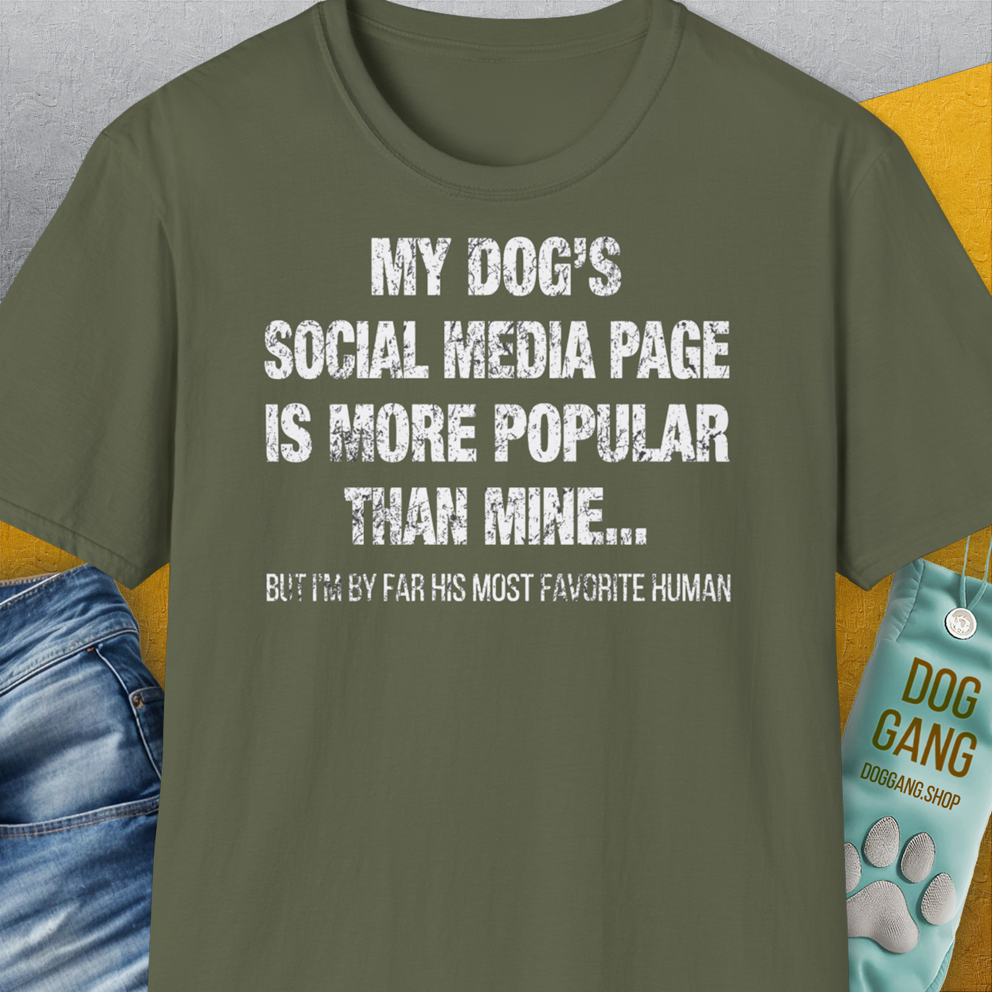 Das Unisex-T-Shirt in Militärgrün besteht aus 100 % Baumwolle und trägt den humorvollen Slogan: „Die Social-Media-Seite meines Hundes ist beliebter als meine.“ Design von Dog Gang.