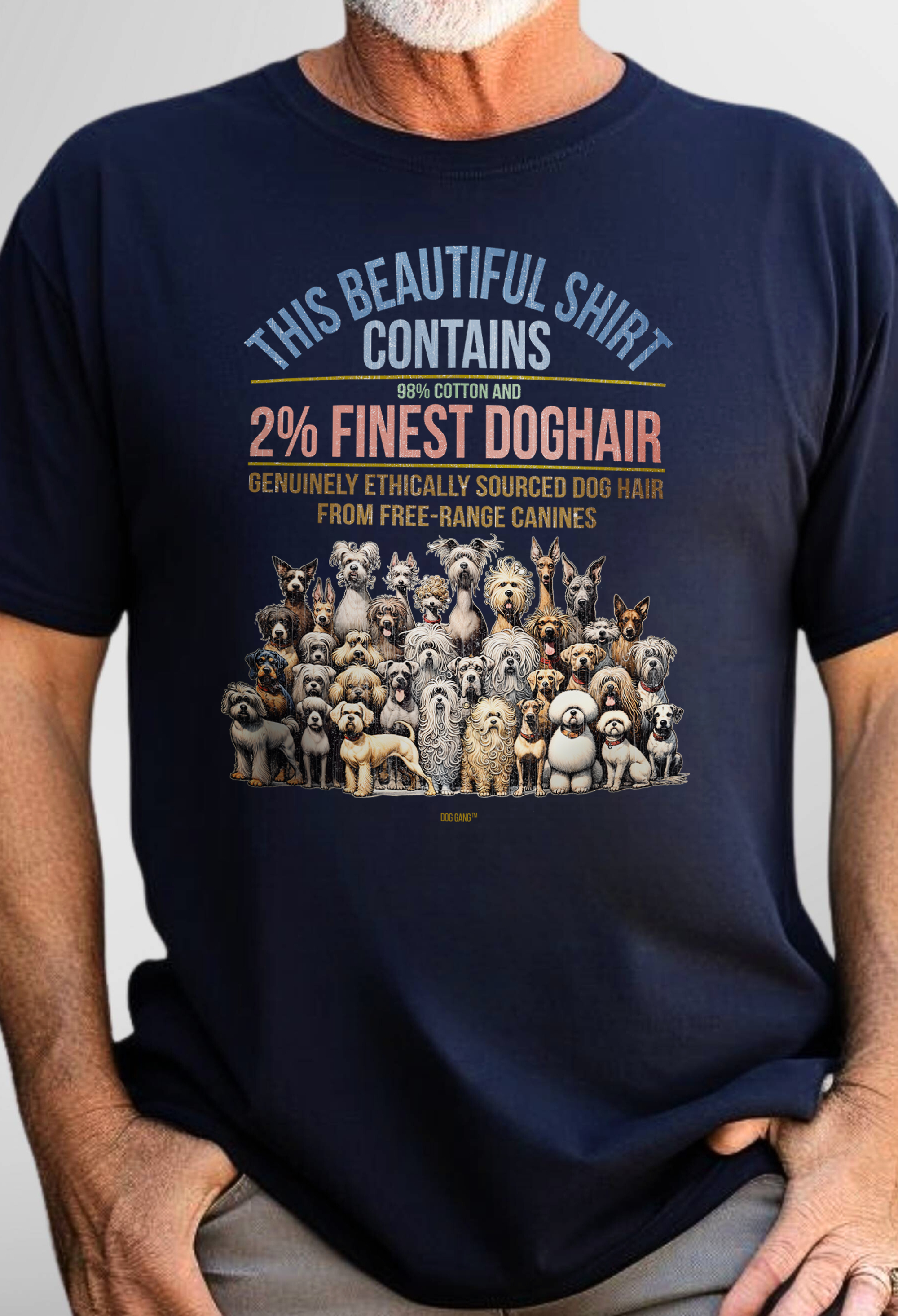 A person wearing a navy blue T-shirt featuring a humorous design with illustrations of various dog breeds. The text reads: This beautiful shirt contains 98% cotton and 2% finest dog hair. Genuinely ethically sourced dog hair from free-range canines. From Dog Gang's "Finest Doghair" series.
