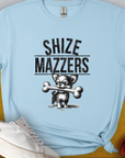 The light blue t-shirt displays a funny cartoon dog holding an oversized bone in its mouth, preventing it from speaking properly. The text reads "SHIZE MAZZERS". Perfect for any dog ​​lover. Designed by Dog Gang.