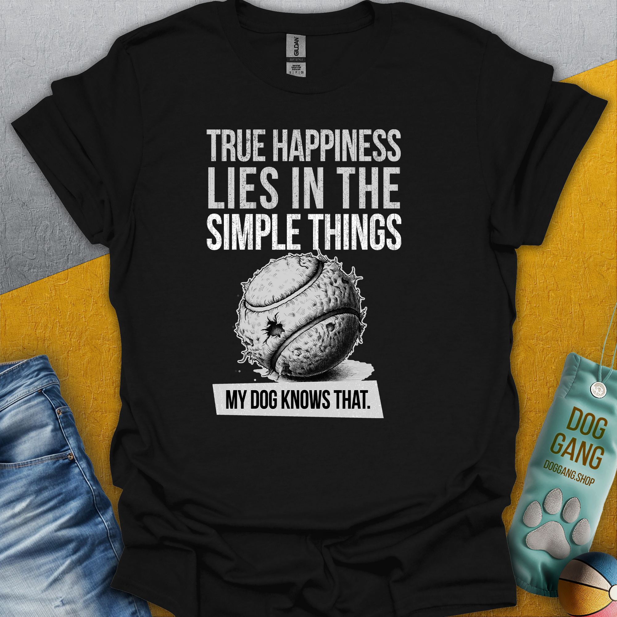 Schwarzes Unisex-T-Shirt aus 100 % Baumwolle mit der Aufschrift „True happiness lies in the simple things - my dog knows that“ und einem Bild eines zerkauten Balls. Design von Dog Gang.