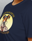 Eine Person trägt das Unisex-T-Shirt „Walking The Dog Every Day Keeps The Doctor Away, Volume 2“ in Marineblau. Es ist mit einem Cartoon-Arzthund und einem verspielten Text versehen und besteht aus 100 % Baumwolle für Komfort und Stil.